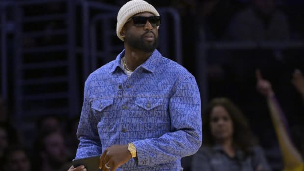 Former Heat guard Dwyane Wade looks on while standing up and watching a game from the sidelines.
